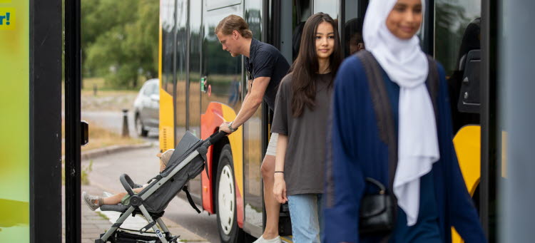 Tre personer går ombord på en buss, en av personerna tar ombord en barnvagn.