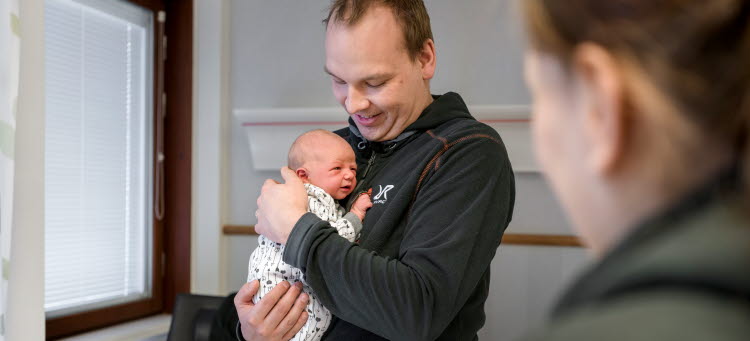 Bild på en pappa som håller sitt nyfödda barn i famnen.