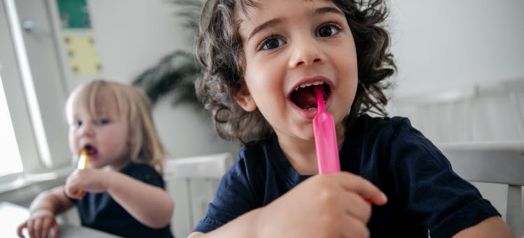 Två barn borstar sina tänder själva vid ett bord på förskolan. 