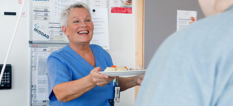 En måltidsvärd serverar mat till en patient på ett sjukhus.