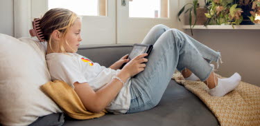 En flicka ligger i soffan och tittar på sin i-pad.